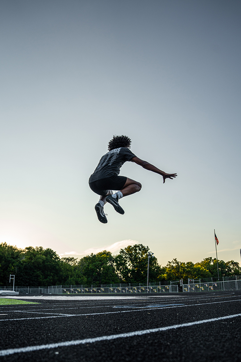 Jalen airborne over the long jump pit at sunset